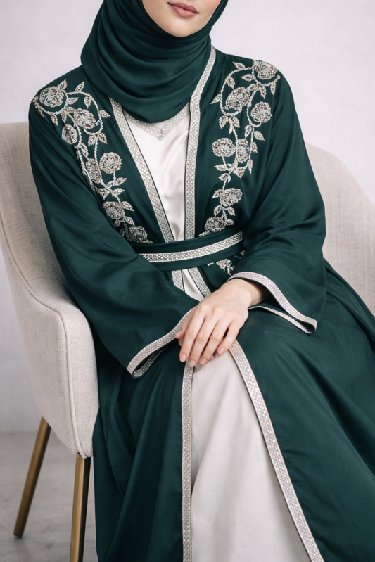 Woman wearing a dark green embroidered abaya sitting on a white chair.