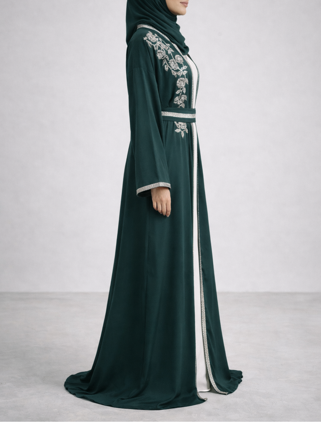 Woman wearing a dark green abaya with white embroidery on a light gray background