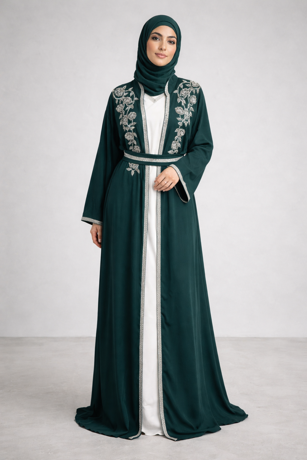 Woman wearing a dark green abaya with white embroidery on a plain background